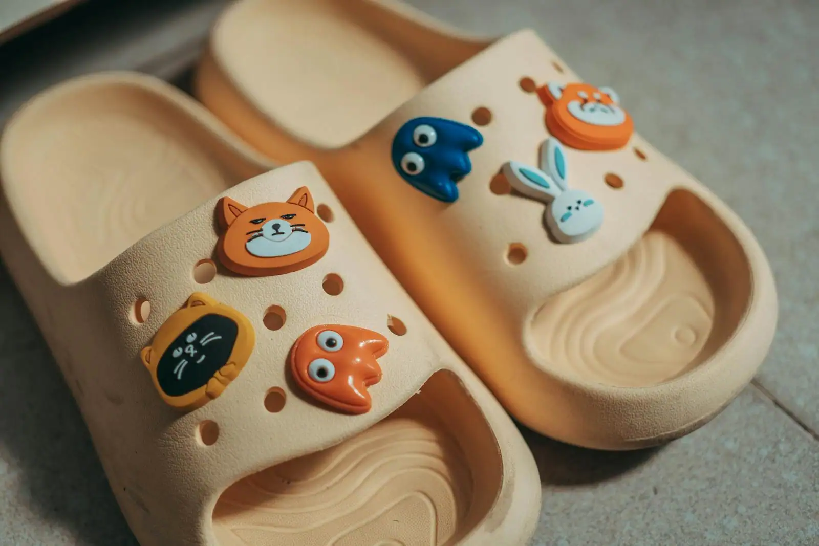 Sabots Crocs colorés décorés de plusieurs breloques Jibbitz clipsées dans les trous, posés sur un sol clair en gros plan
