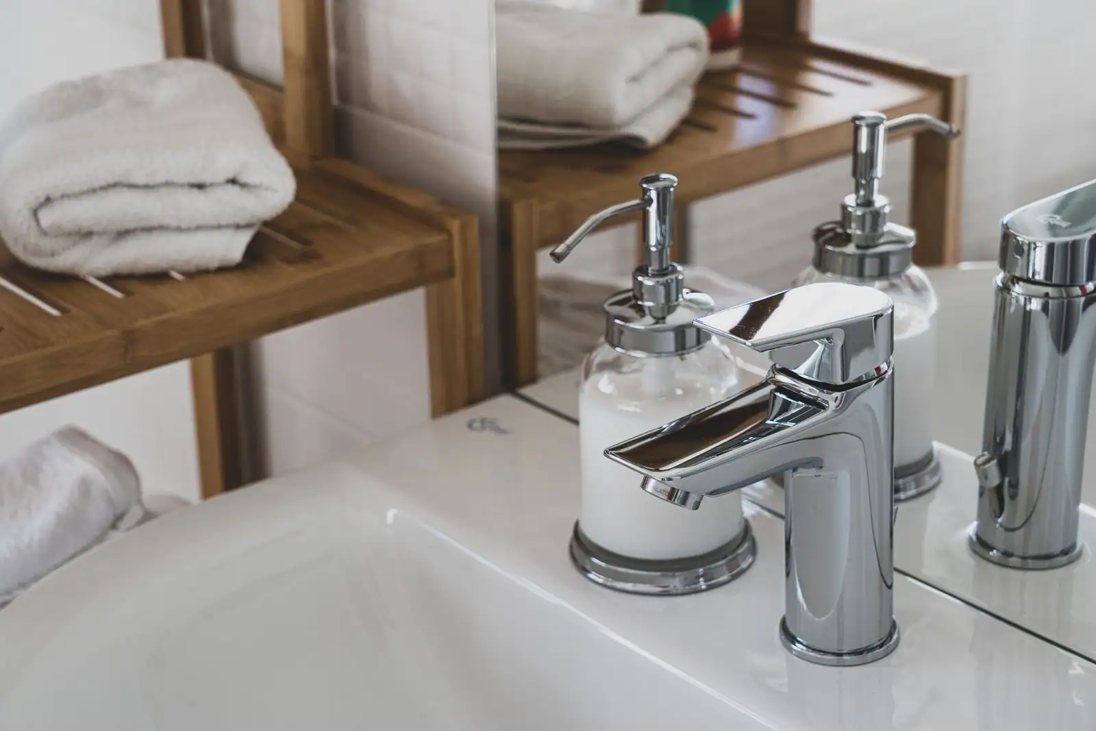 Robinet chromé, distributeur de savon et serviettes blanches pliées sur une étagère en bois de salle de bain.