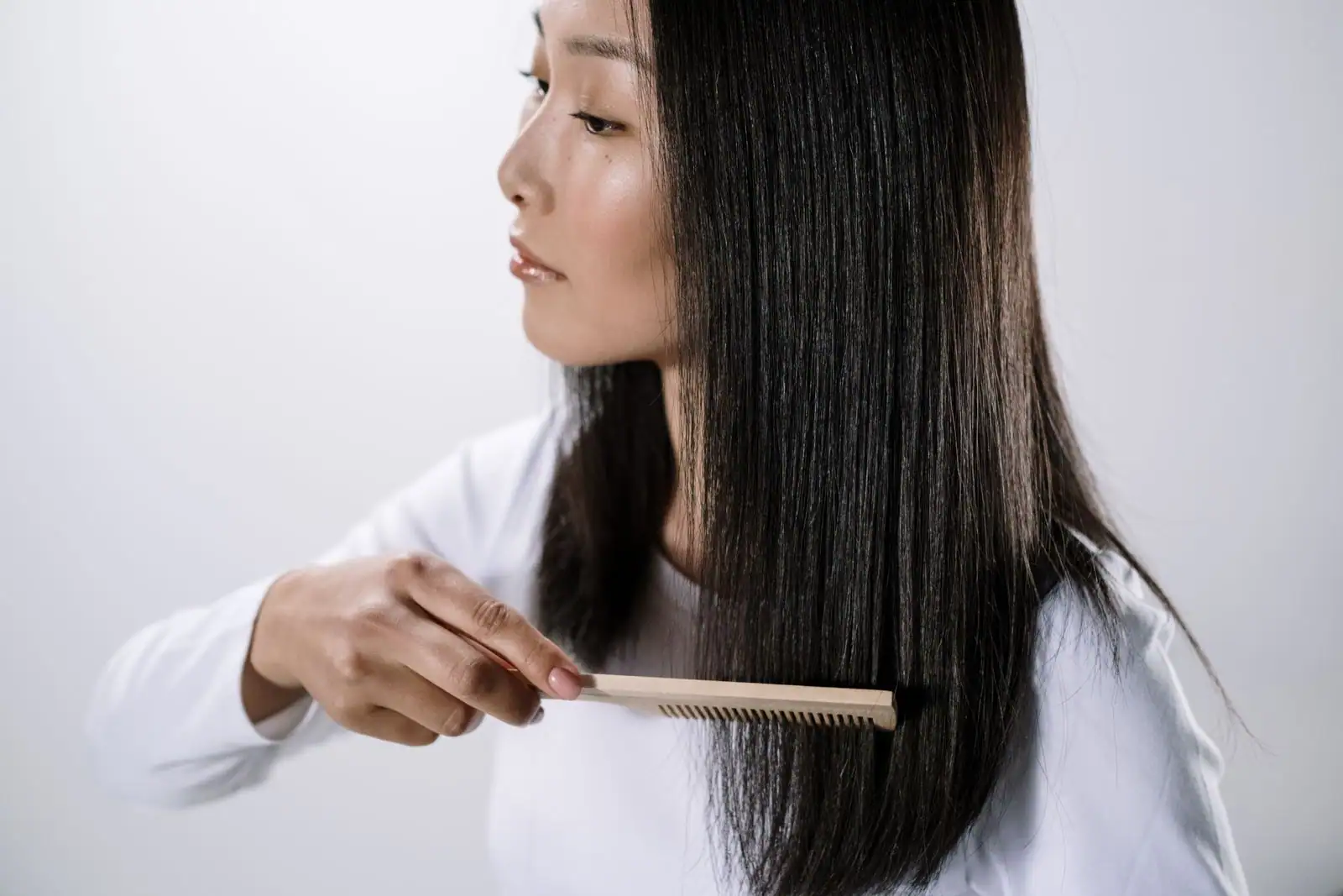 Femme aux longs cheveux lisses et brillants se coiffant au peigne, sur un fond clair