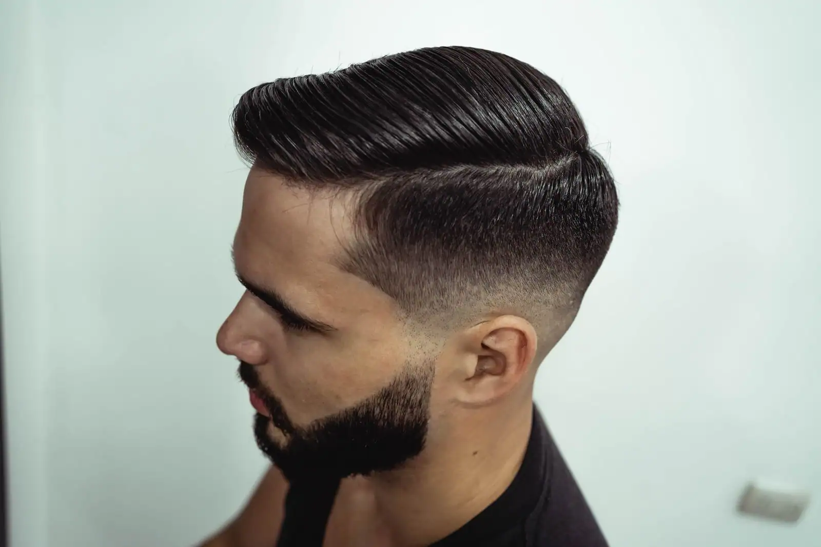 Homme aux côtés rasés en dégradé et au dessus coiffé vers le haut, vu de profil chez le coiffeur