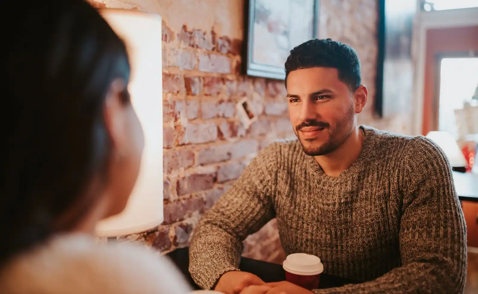Un homme souriant écoute une femme à la table d'un café, ambiance complice de conversation