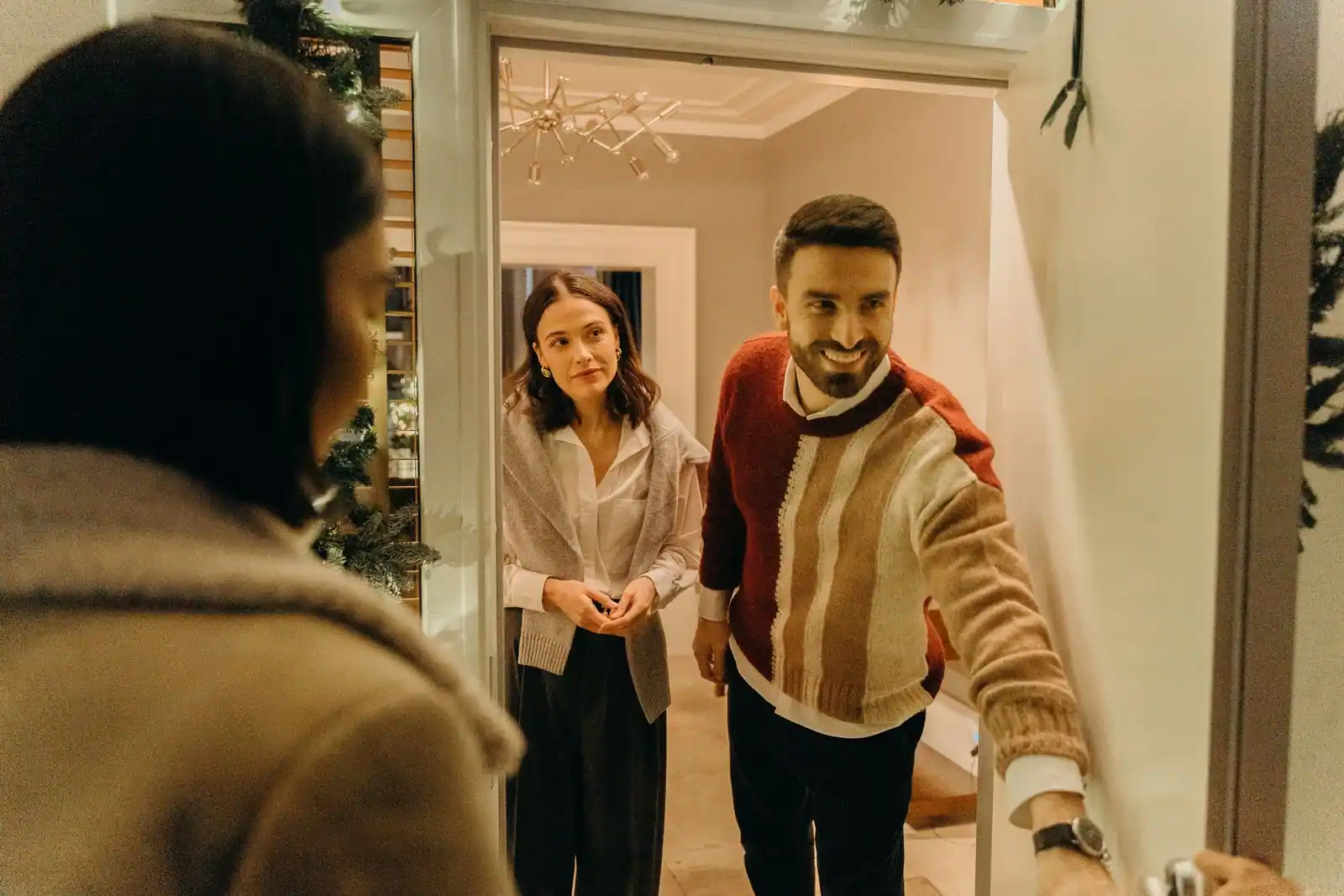Un homme souriant ouvre sa porte pour accueillir une visiteuse, scène conviviale sur le pas de la porte