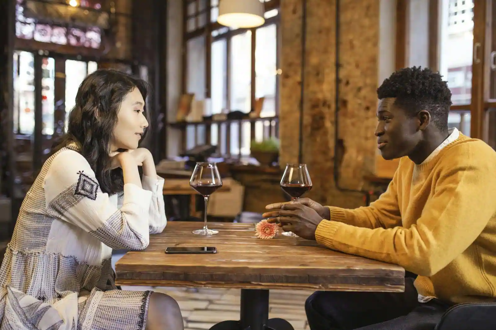 Un homme et une femme en tête-à-tête à une table, deux verres devant eux, en pleine conversation