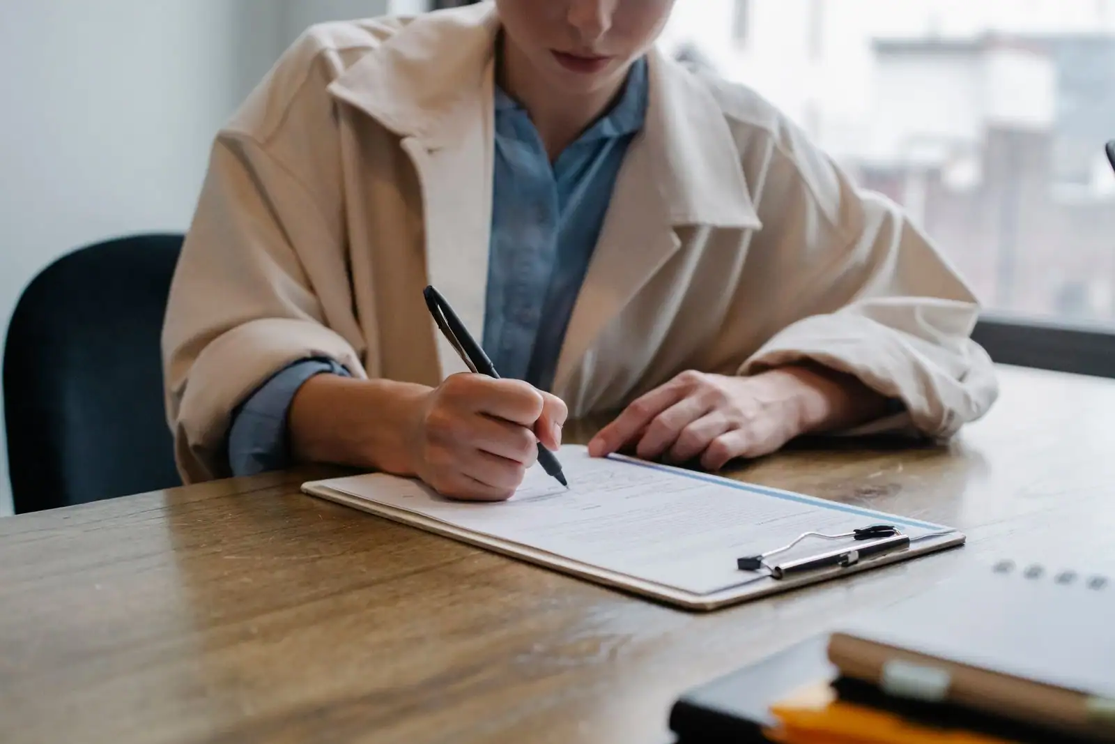 Une jeune femme remplit un document de candidature à un bureau, un stylo à la main.