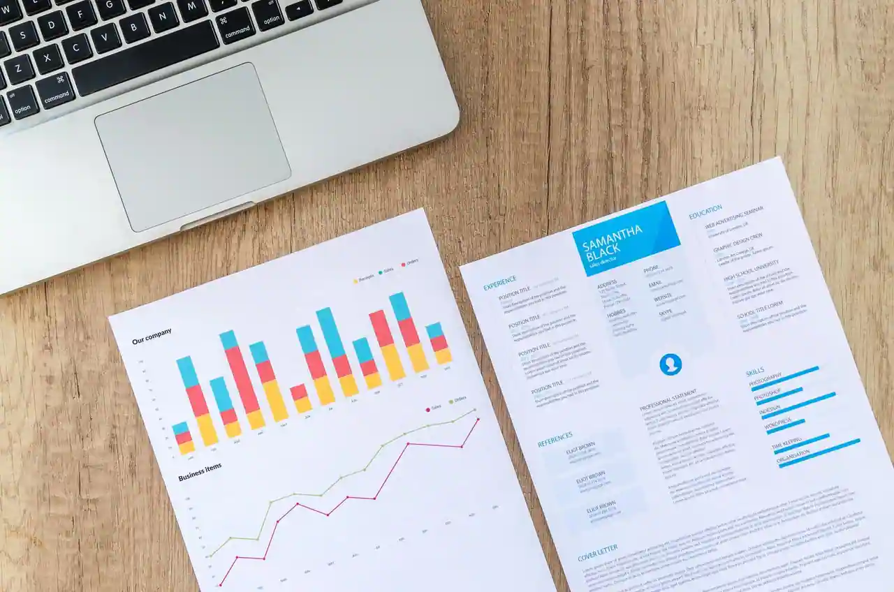 CV imprimé posé sur un bureau en bois, à côté d'un ordinateur portable et d'un graphique d'activité