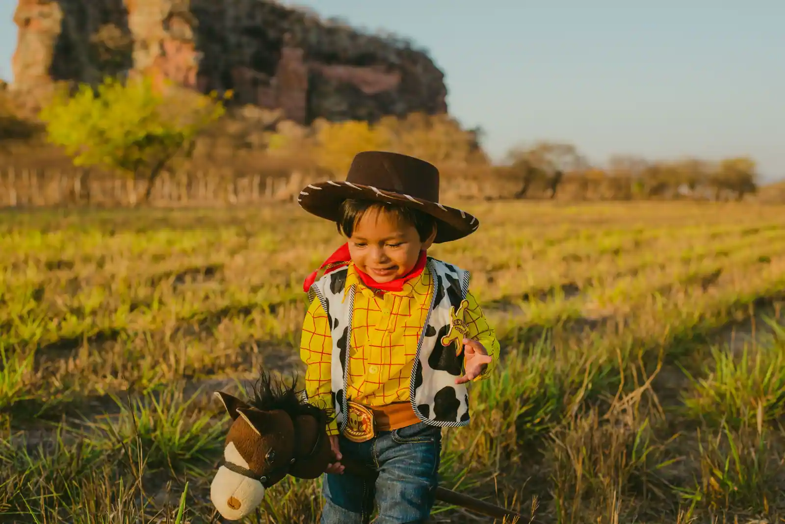 Enfant chevauchant un cheval-bâton à tête en peluche dans un champ au soleil couchant.