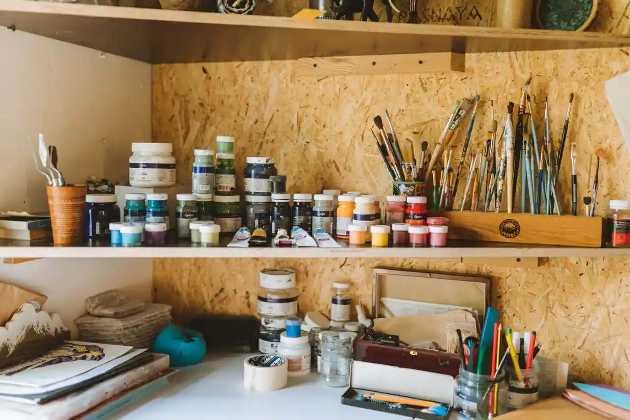 Étagères de fournitures de loisirs créatifs : pots de peinture, pinceaux et crayons de couleur dans un atelier.