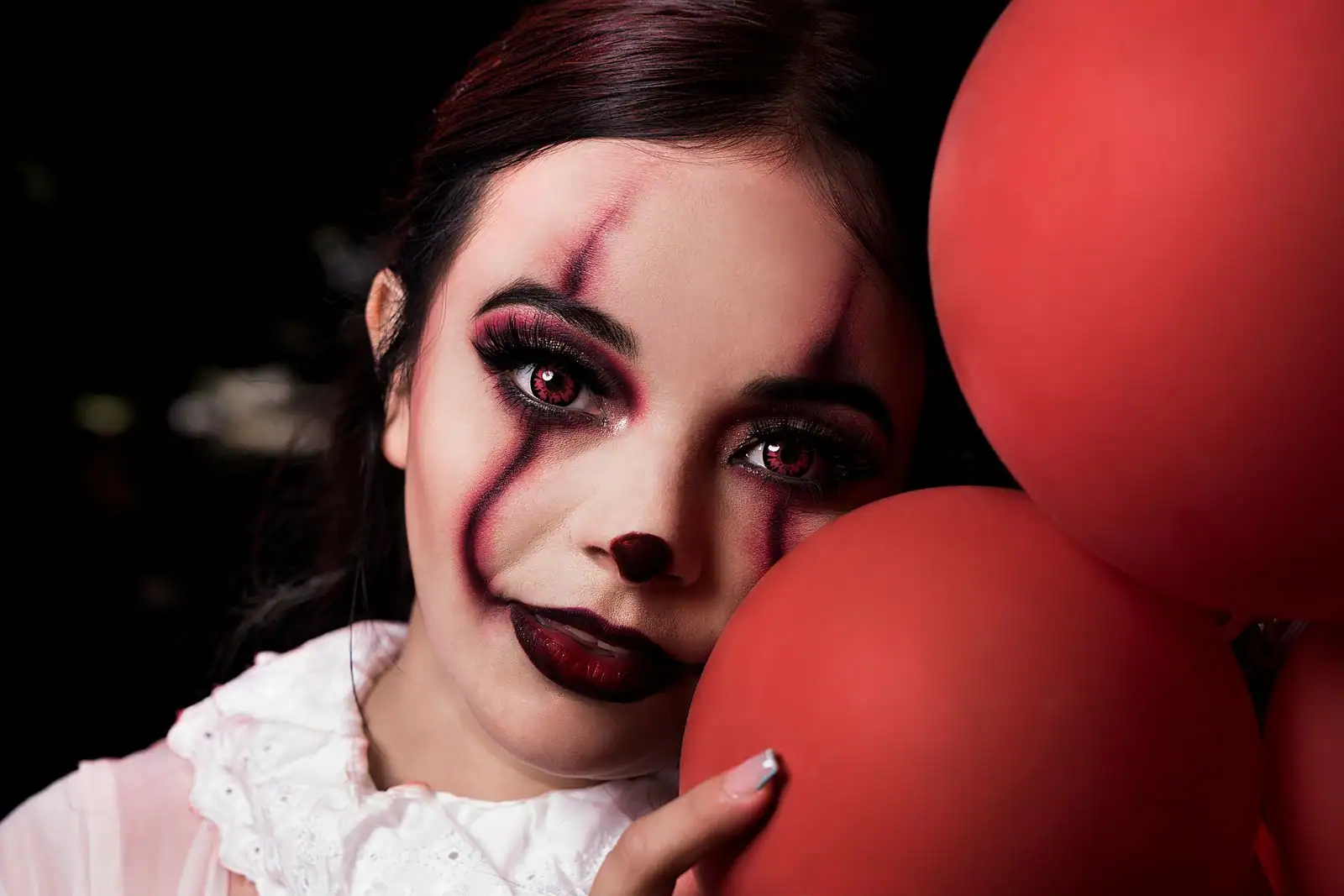Visage maquillé en clown théâtral au teint blanc, yeux noirs charbonneux et large bouche rouge