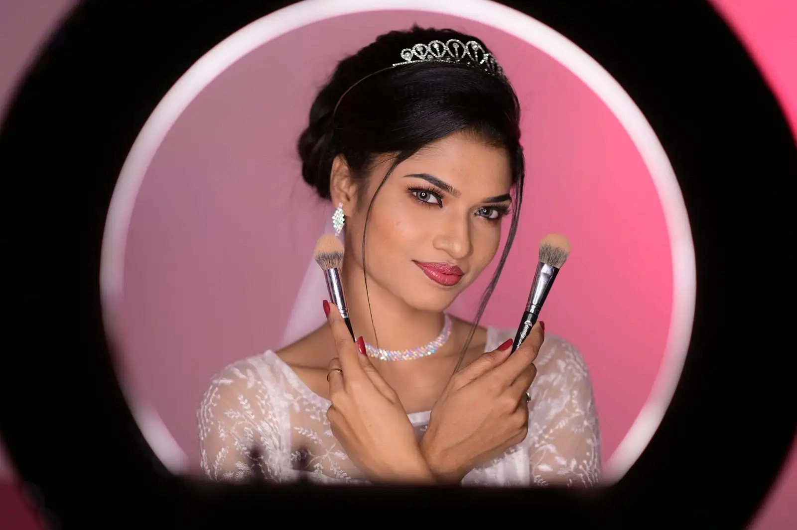 Jeune mariée en diadème tenant deux pinceaux de maquillage, portrait en gros plan.