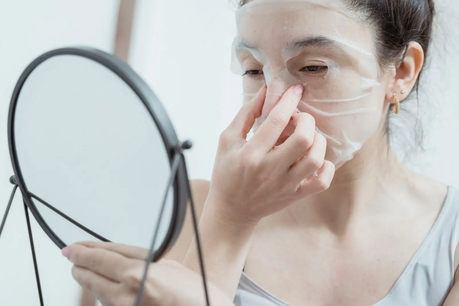 Jeune femme ajustant un masque de soin en tissu sur son visage devant un miroir