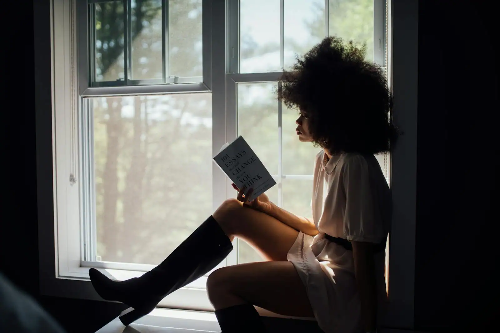 Une femme lit un livre, installée au calme près d'une fenêtre lumineuse