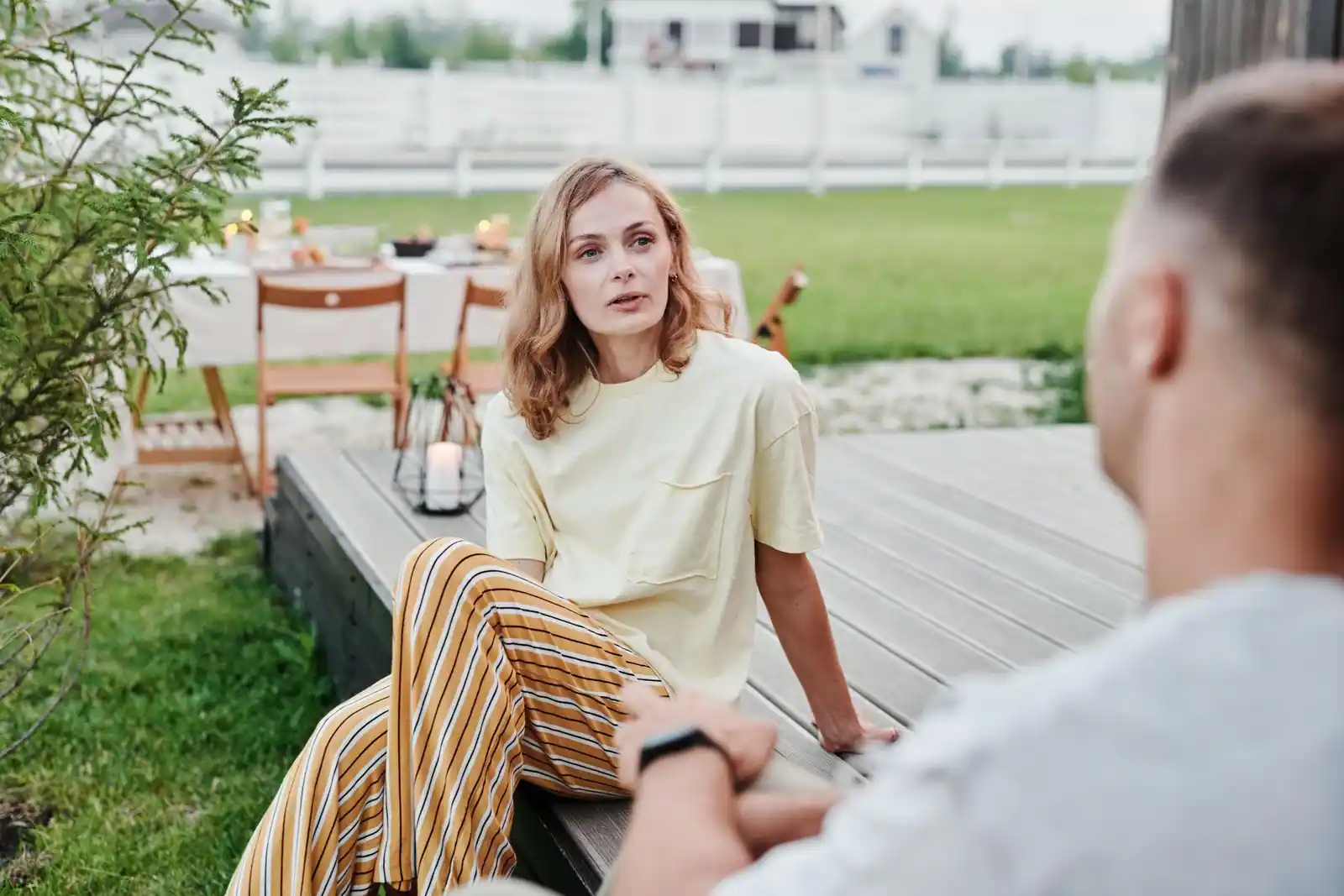 Couple en extérieur sur une terrasse en bois, en pleine conversation dans une lumière douce de jardin