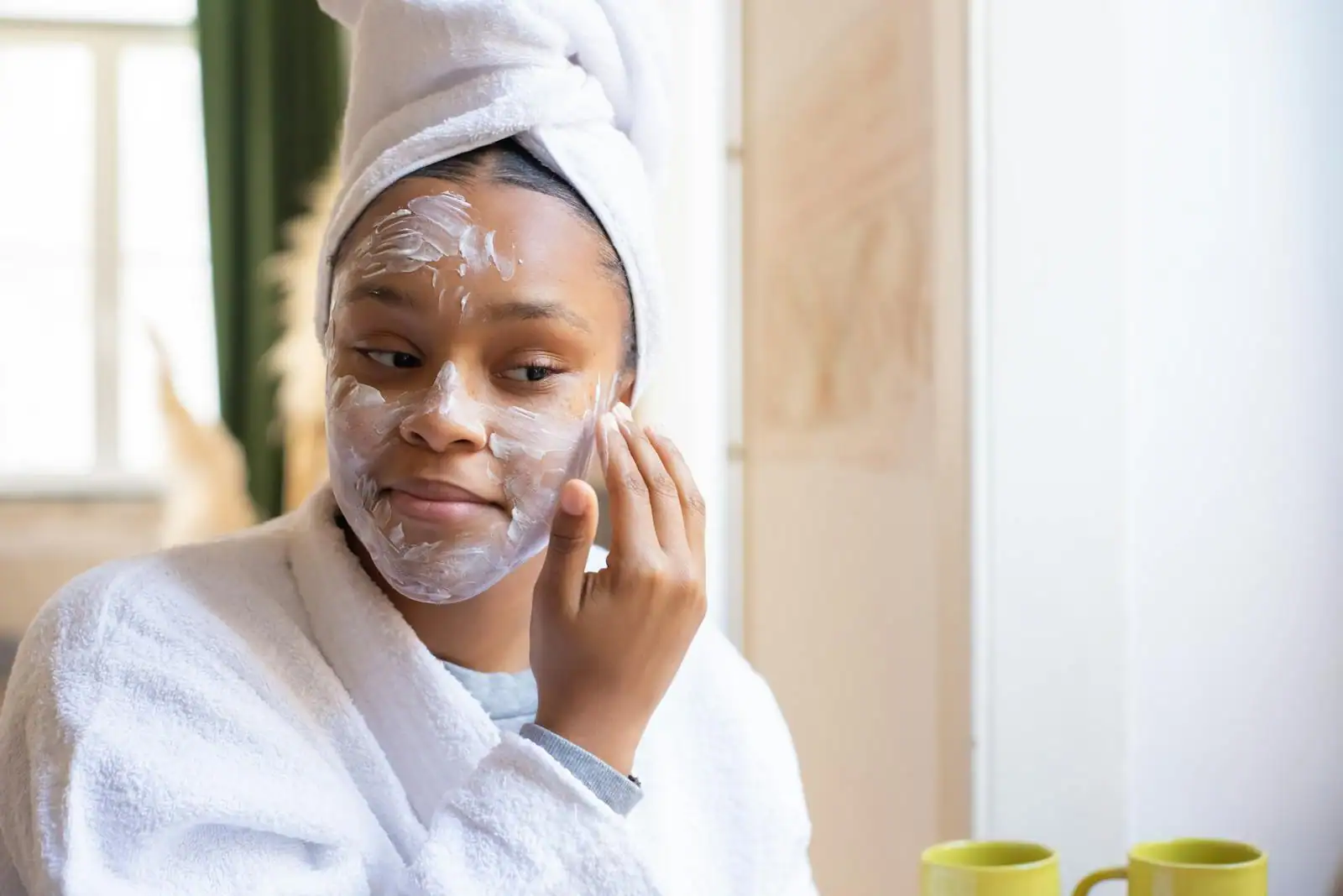 Jeune femme appliquant un soin hydratant sur son visage devant un miroir, lumière naturelle, routine beauté du matin.