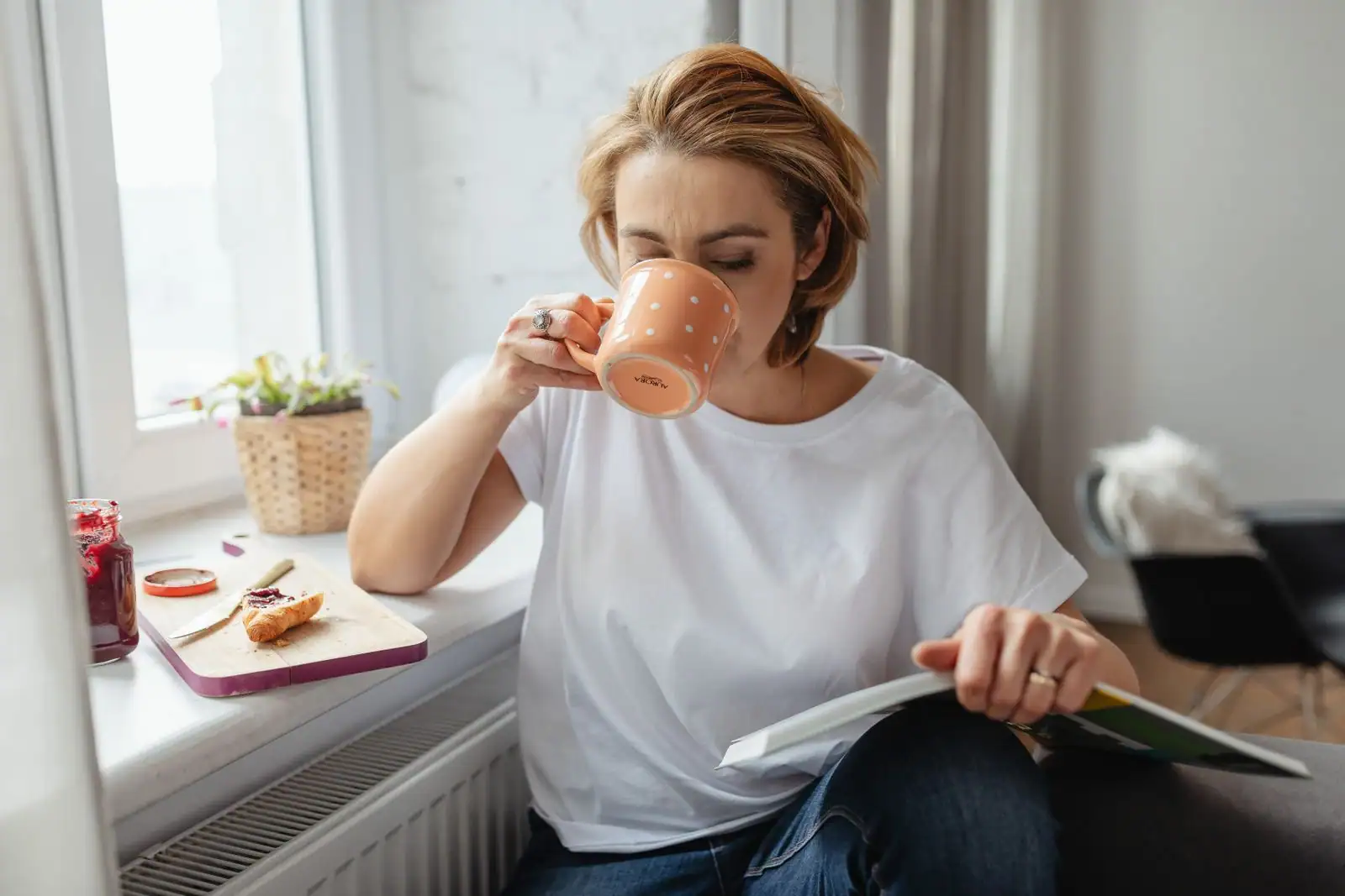 Femme à sa fenêtre le matin, tasse à la main, dans une ambiance calme