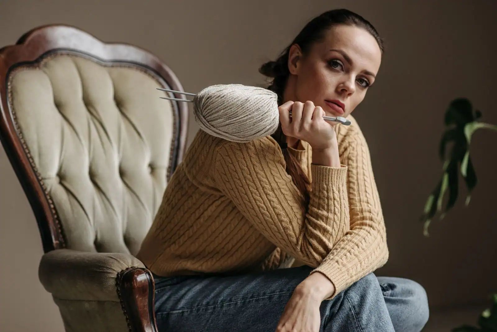 Femme en pull beige à grosse maille torsadée, assise dans un fauteuil avec une pelote de laine