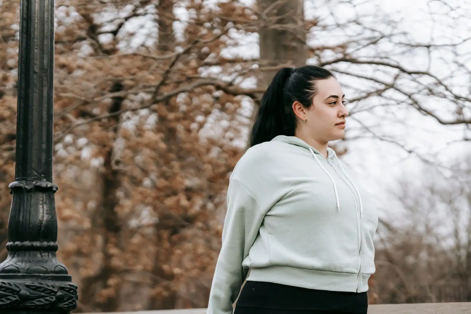 Jeune femme grande taille en sweat à capuche clair, en extérieur dans un parc