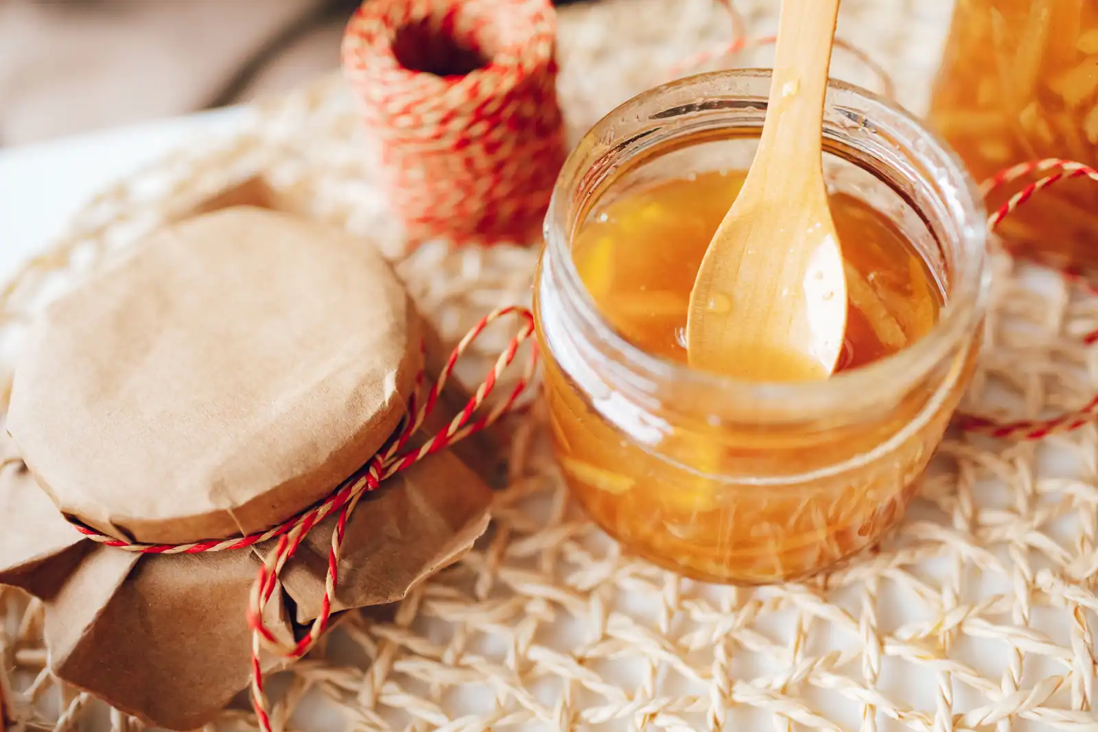 Pot de confiture dorée maison et sa cuillère en bois, aux filaments baignés dans un sirop ambré