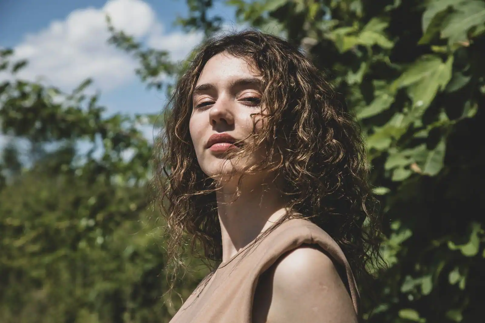 Femme aux cheveux bouclés bruns volumineux et bien définis, en extérieur dans une lumière naturelle ensoleillée