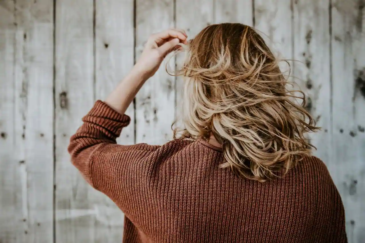Femme vue de dos aux cheveux mi-longs ondulés, plus foncés aux racines et blonds vers les pointes