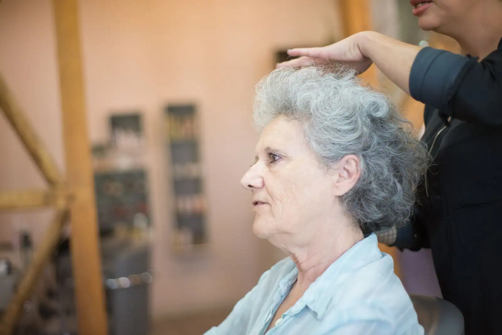 Femme aux cheveux poivre et sel argentés et bouclés, coiffée en salon, mèches claires et foncées.