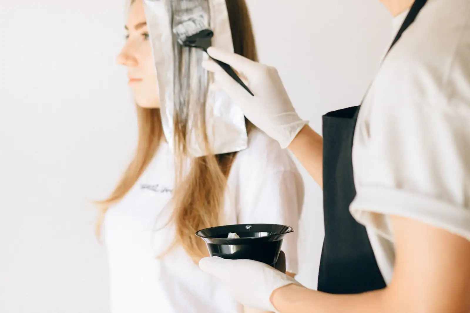 Application d'une coloration au pinceau sur cheveux longs, avec gants et bol de teinture.