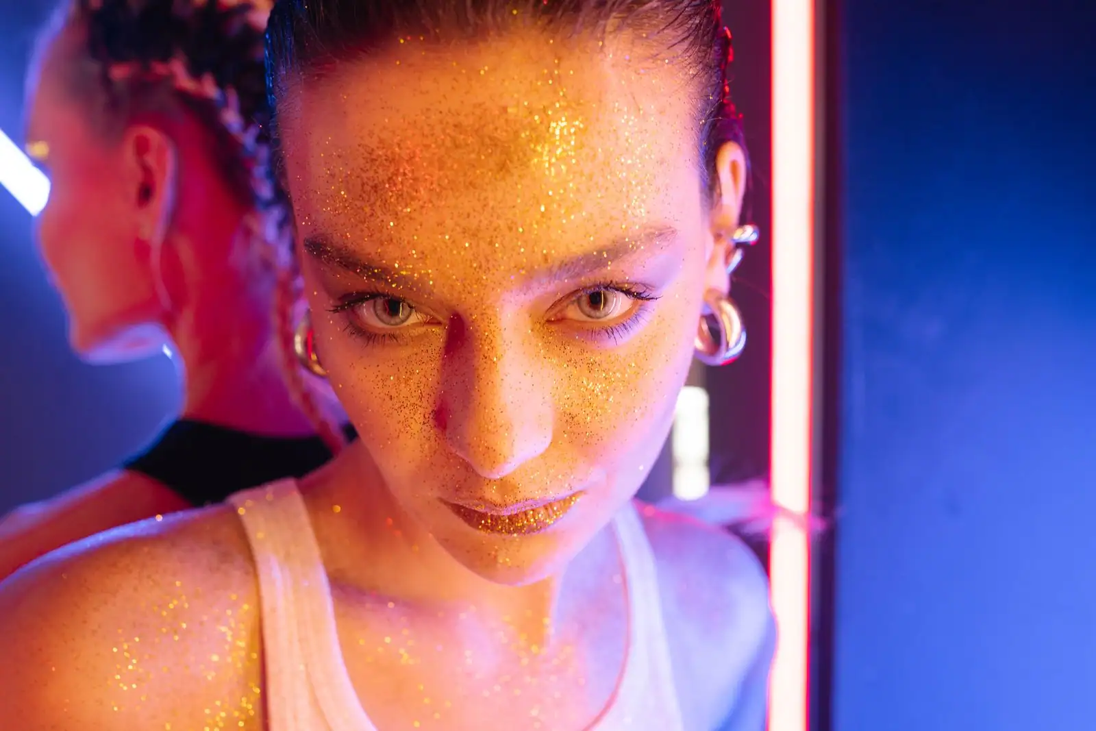 Femme au visage constellé de paillettes dorées sous des lumières colorées, dans une ambiance de fête disco.