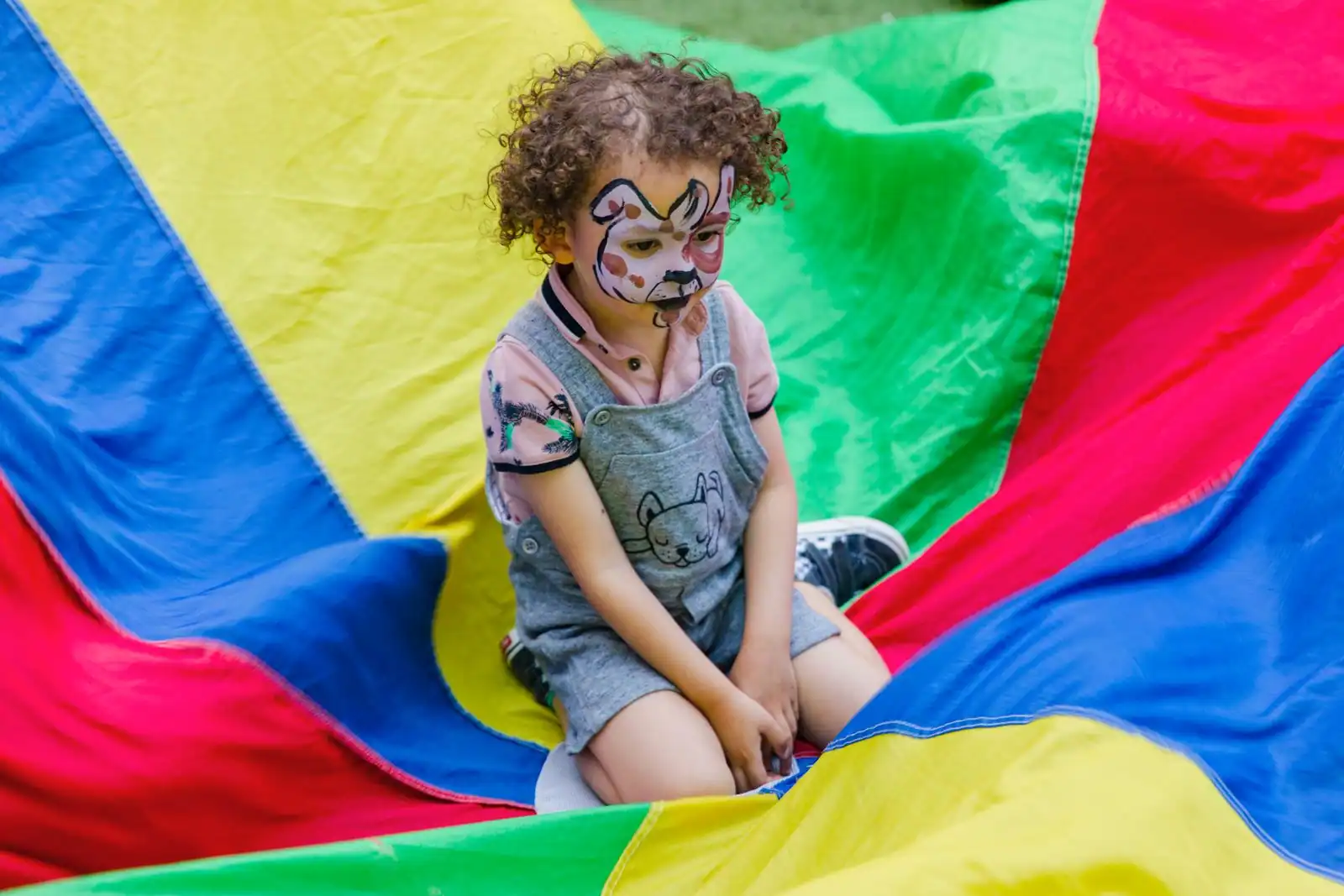 Jeune enfant au visage maquillé en animal, assis sur une grande toile de jeu aux couleurs vives