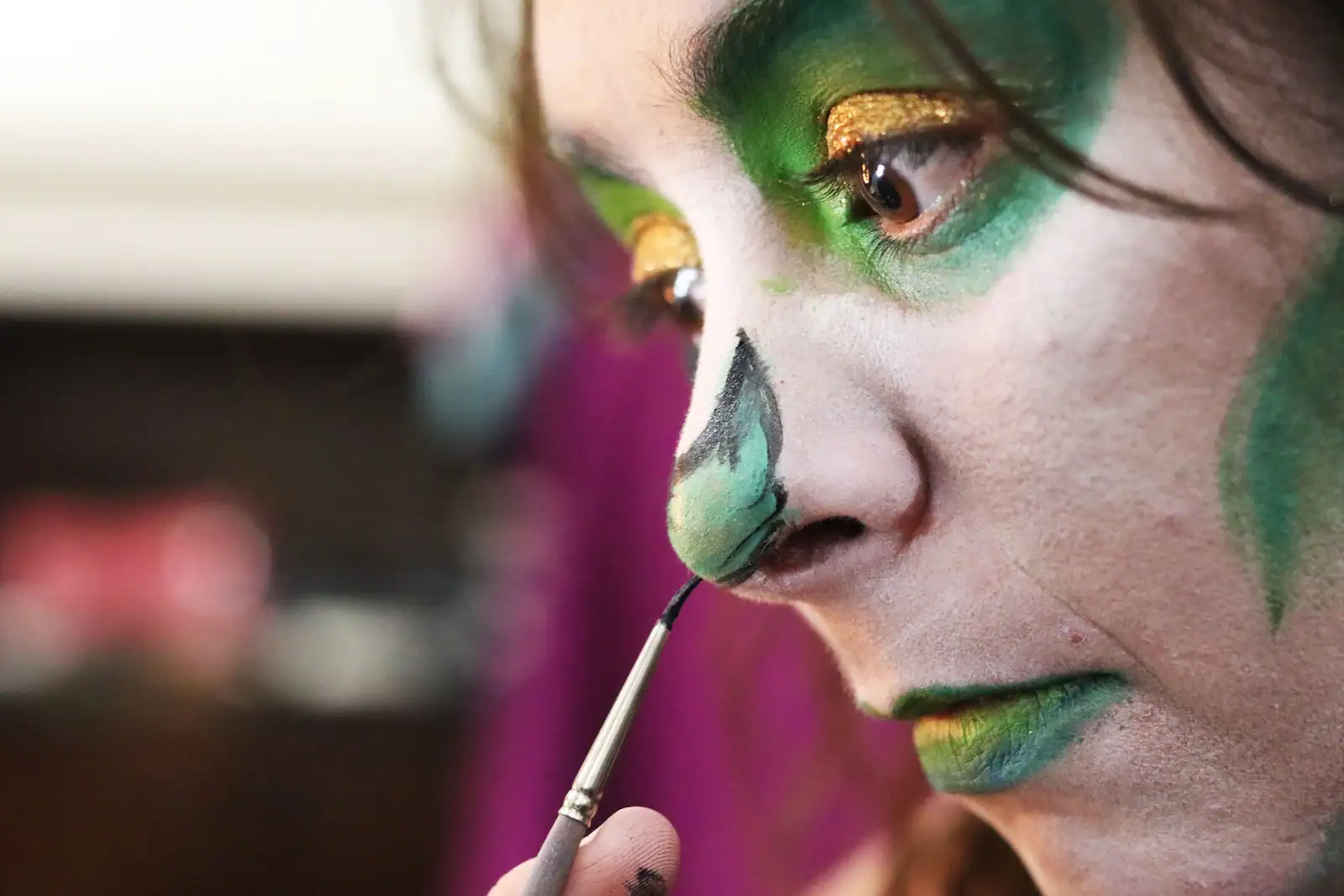 Gros plan d’un visage maquillé de vert appliqué au pinceau, dans une ambiance de déguisement