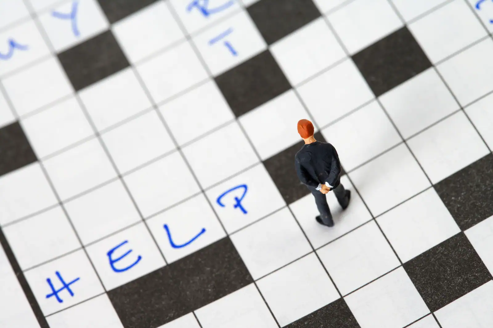 Grille de mots croisés en gros plan avec une figurine posée dessus et quelques lettres inscrites.