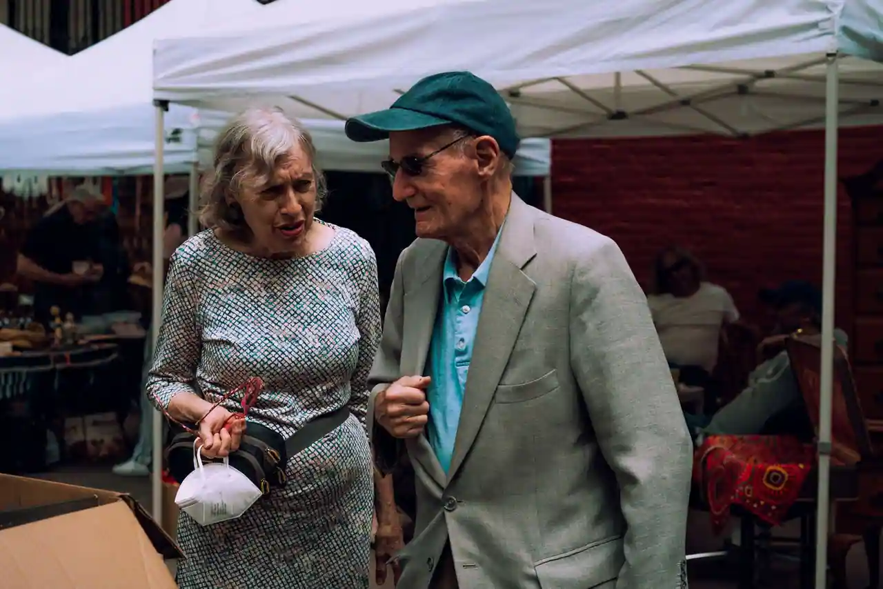 Un couple de personnes âgées flâne parmi les stands blancs d'un marché de brocante en plein air