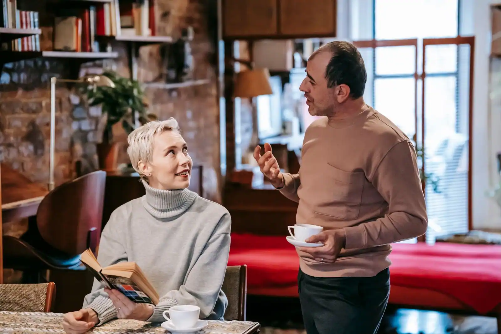 Couple d'âge mûr en conversation à la maison, un livre et deux tasses de café dans un intérieur chaleureux.