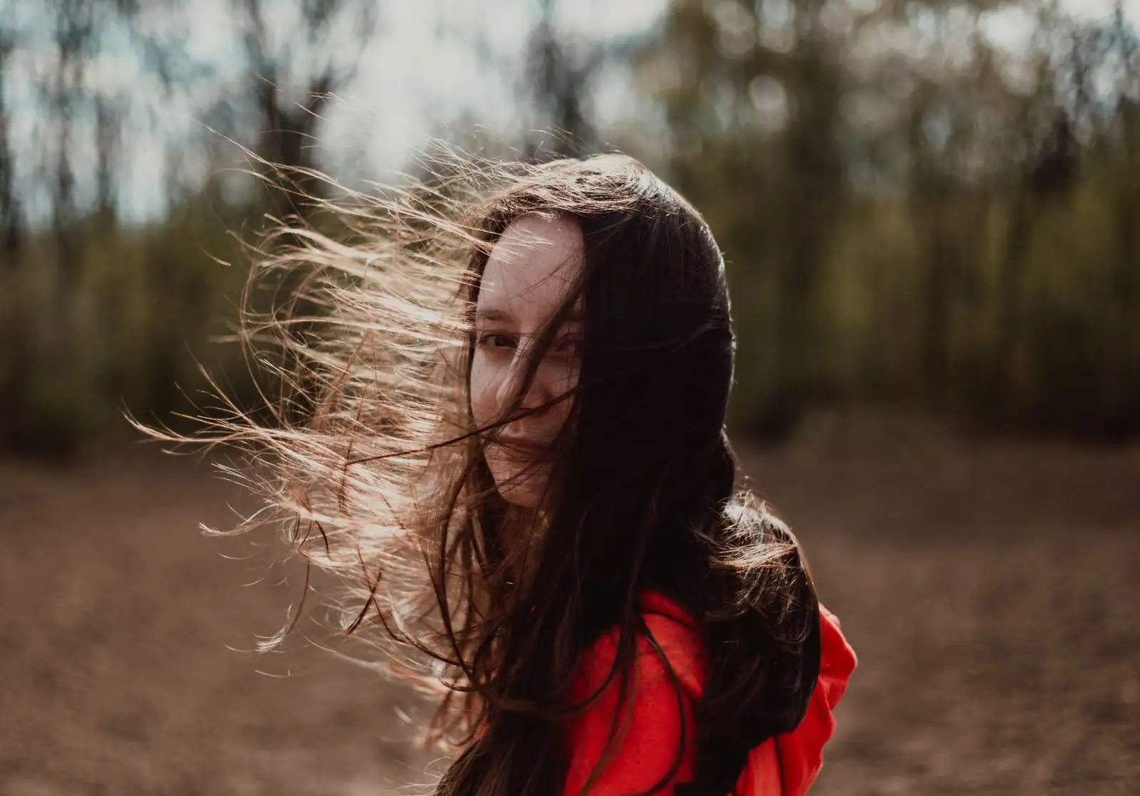 Femme aux longs cheveux bruns dont le vent soulève des mèches en travers du visage, dehors à contre-jour