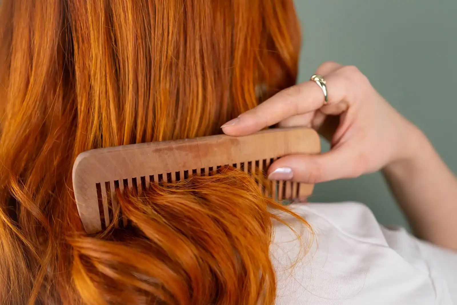 Femme démêlant ses longs cheveux roux avec un peigne en bois, mèches fines qui s'échappent encore