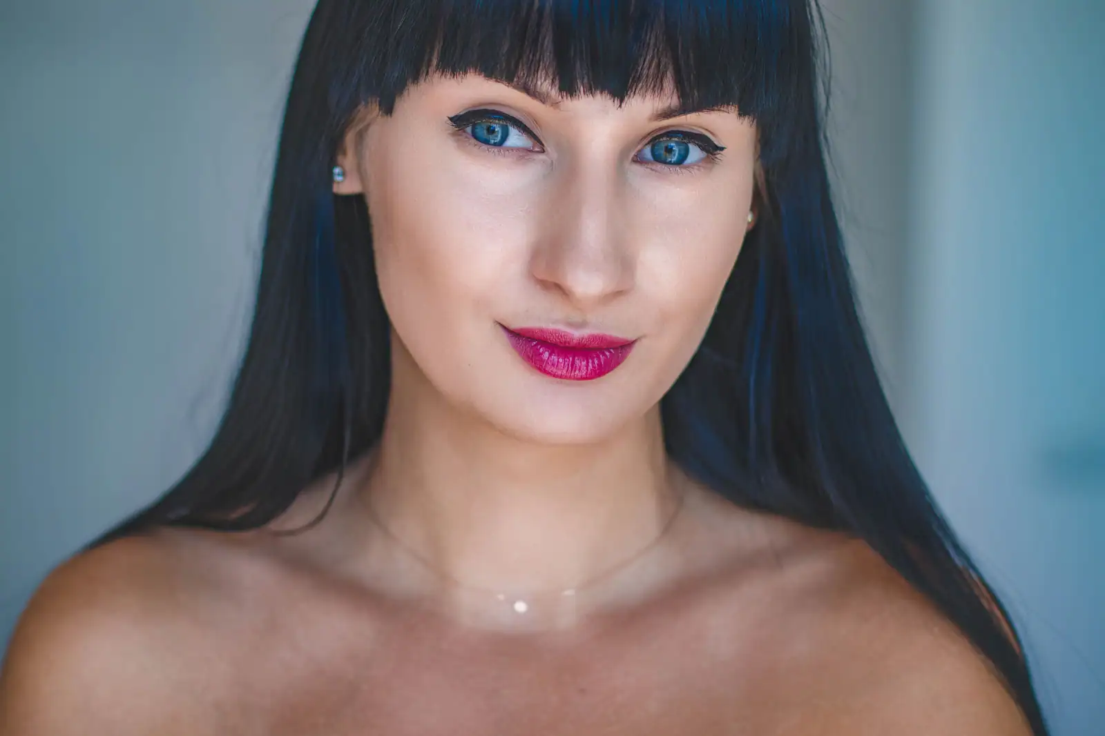 Femme aux cheveux noirs lisses à reflets bleutés et frange droite, contrastant avec sa peau claire