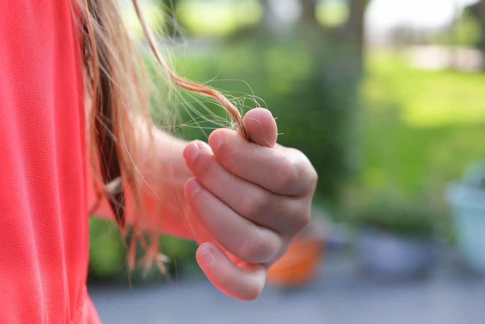 Main tenant une mèche de cheveux clairs dont les pointes fourchues se détachent en fins filaments