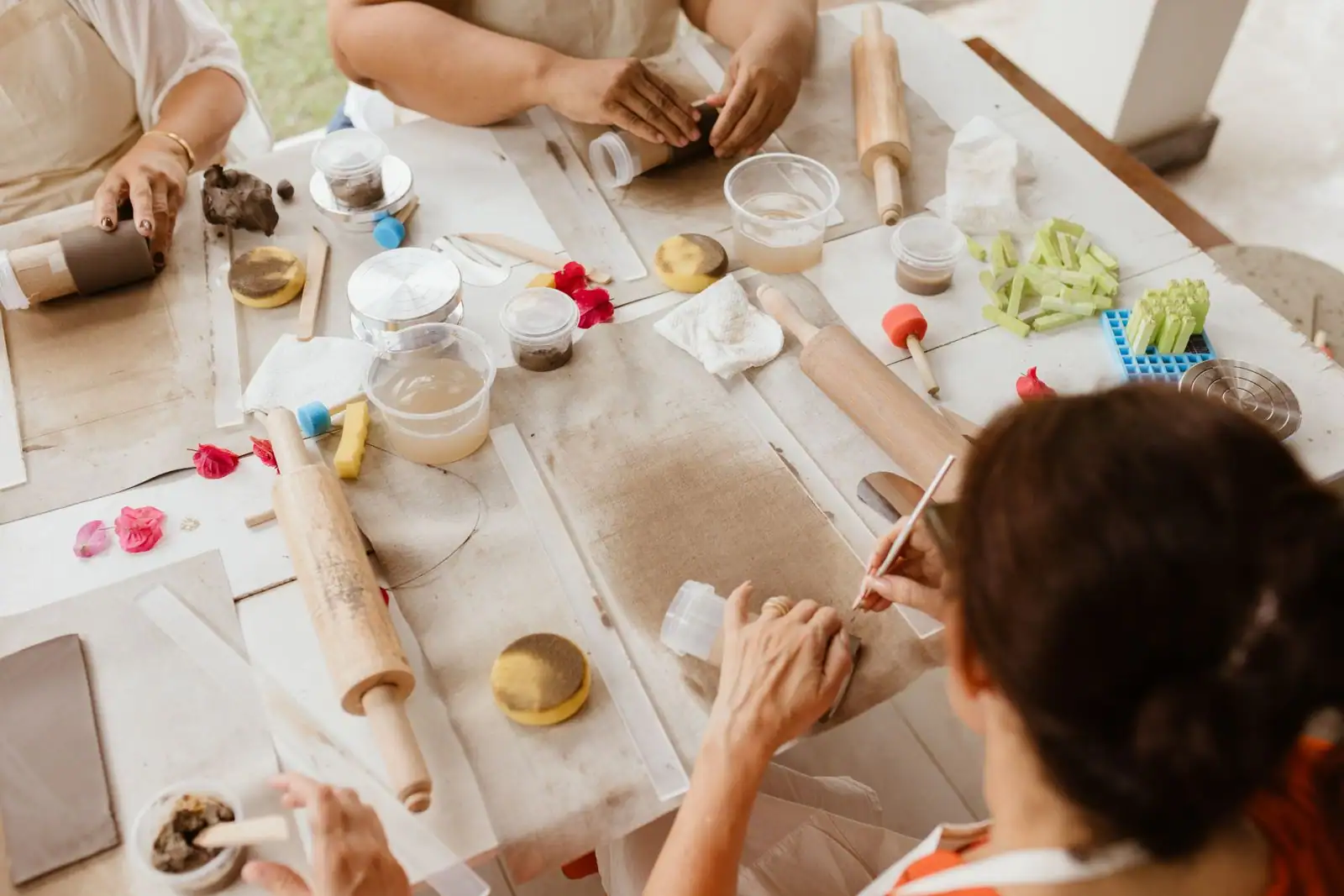 Adultes réunis autour d'une table d'atelier de céramique, façonnant l'argile au rouleau
