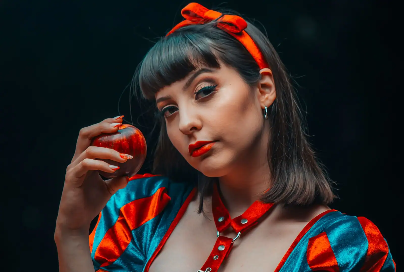 Femme en costume de Blanche-Neige, bandeau rouge à nœud et bouche rouge nette, une pomme à la main