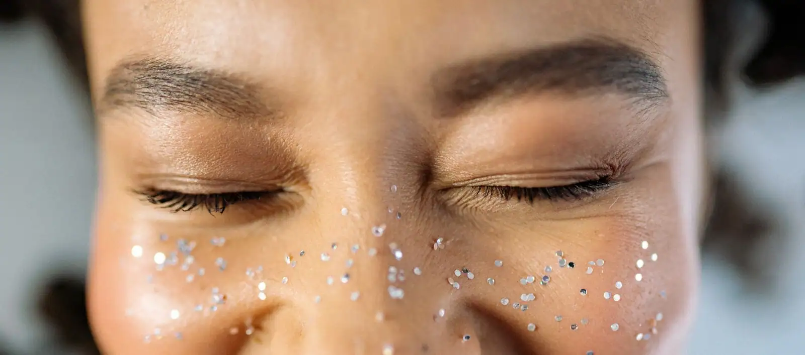 Gros plan sur un visage aux yeux fermés et de fines paillettes argentées dispersées sur les pommettes