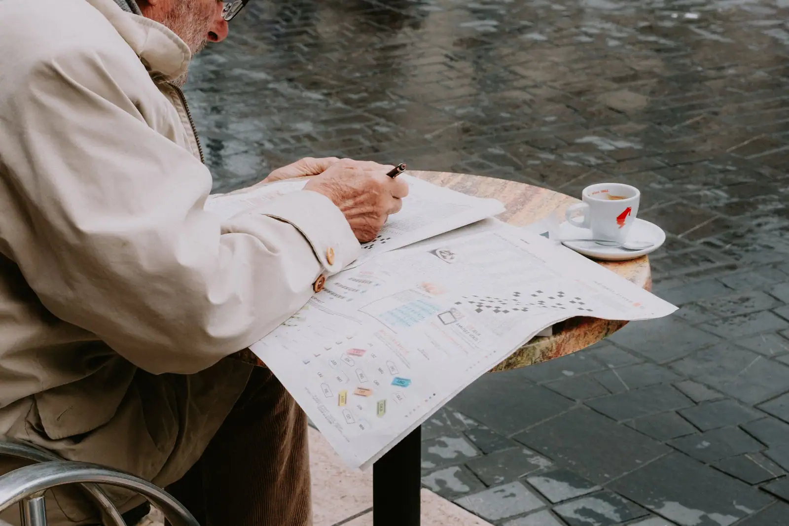 Homme attablé à la terrasse d'un café, stylo en main, remplissant la grille de jeux d'un journal